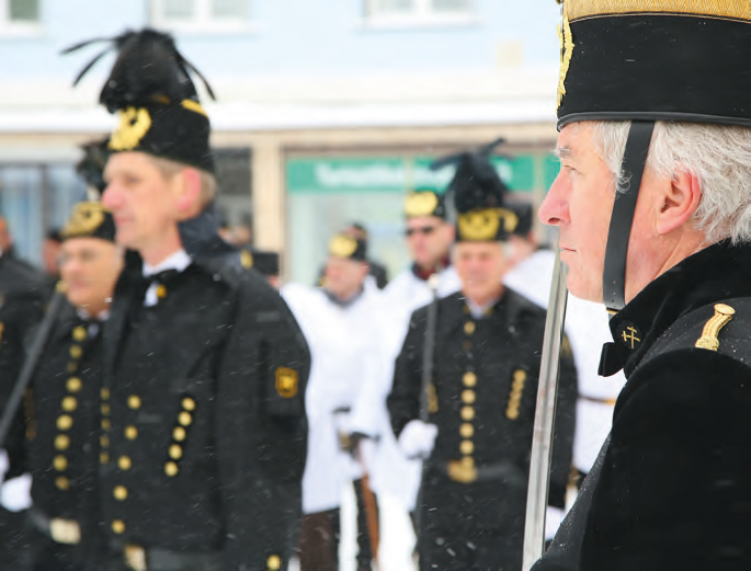 An older man in a black and gold traditional uniform stands in profile during a formal winter parade.