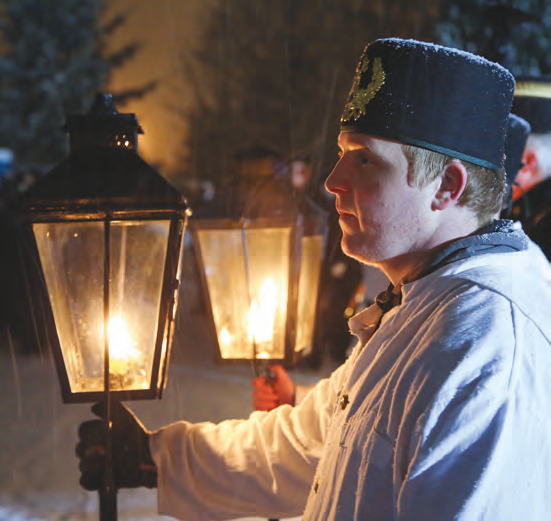 A man dressed in traditional attire holds a burning lantern during a nighttime outdoor ceremony in winter.