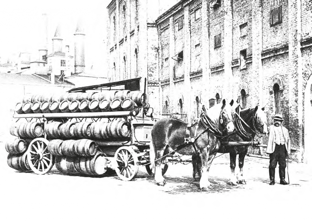 Historical black-and-white photograph of a brewery delivery scene featuring a horse-drawn wagon loaded with multiple rows of wooden beer barrels.